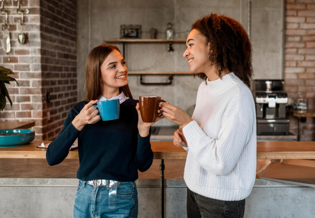 Duas mulheres sorridentes tomando café em canecas, demonstrando a resistência das lentes de contato dental na Clínica Dahdal Aoun.