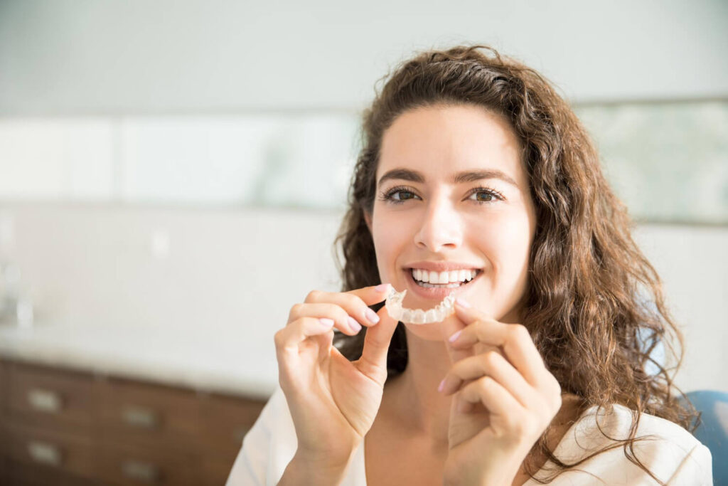 Paciente sorridente segura alinhador transparente Invisalign em Moema na Dahdal Aoun, demonstrando a praticidade de remover o aparelho.