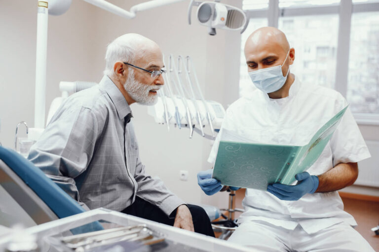 Dentista analisa exames de periodontite com paciente idoso para explicar a recuperação de osso na Dahdal Aoun Odontologia em Moema.