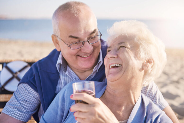 Casal idoso sorrindo alegremente ao ar livre, refletindo a segurança do implante dentário em Moema para pacientes com osteoporose.